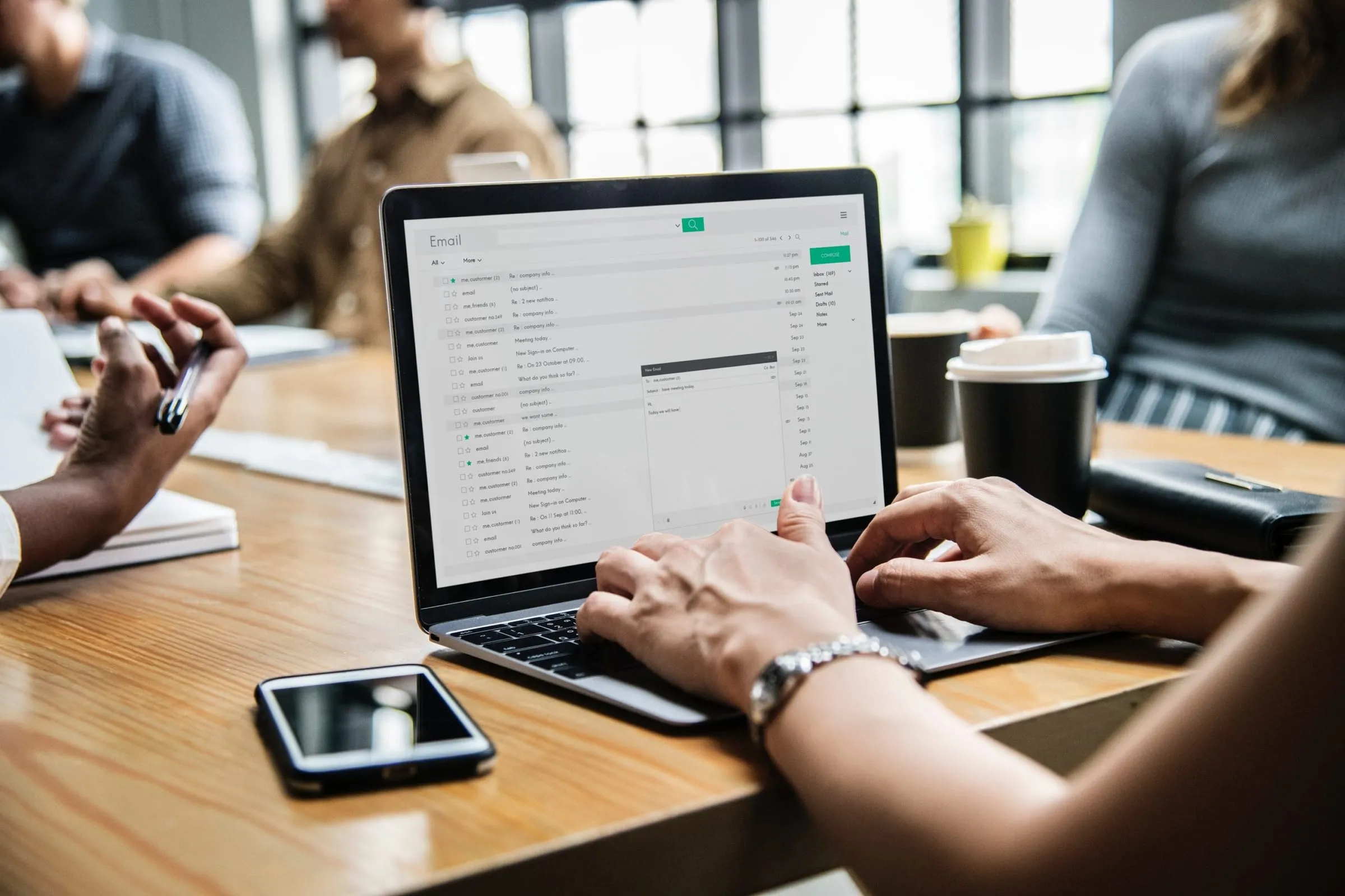 Hands typing on a laptop showing an email inbox at a meeting table