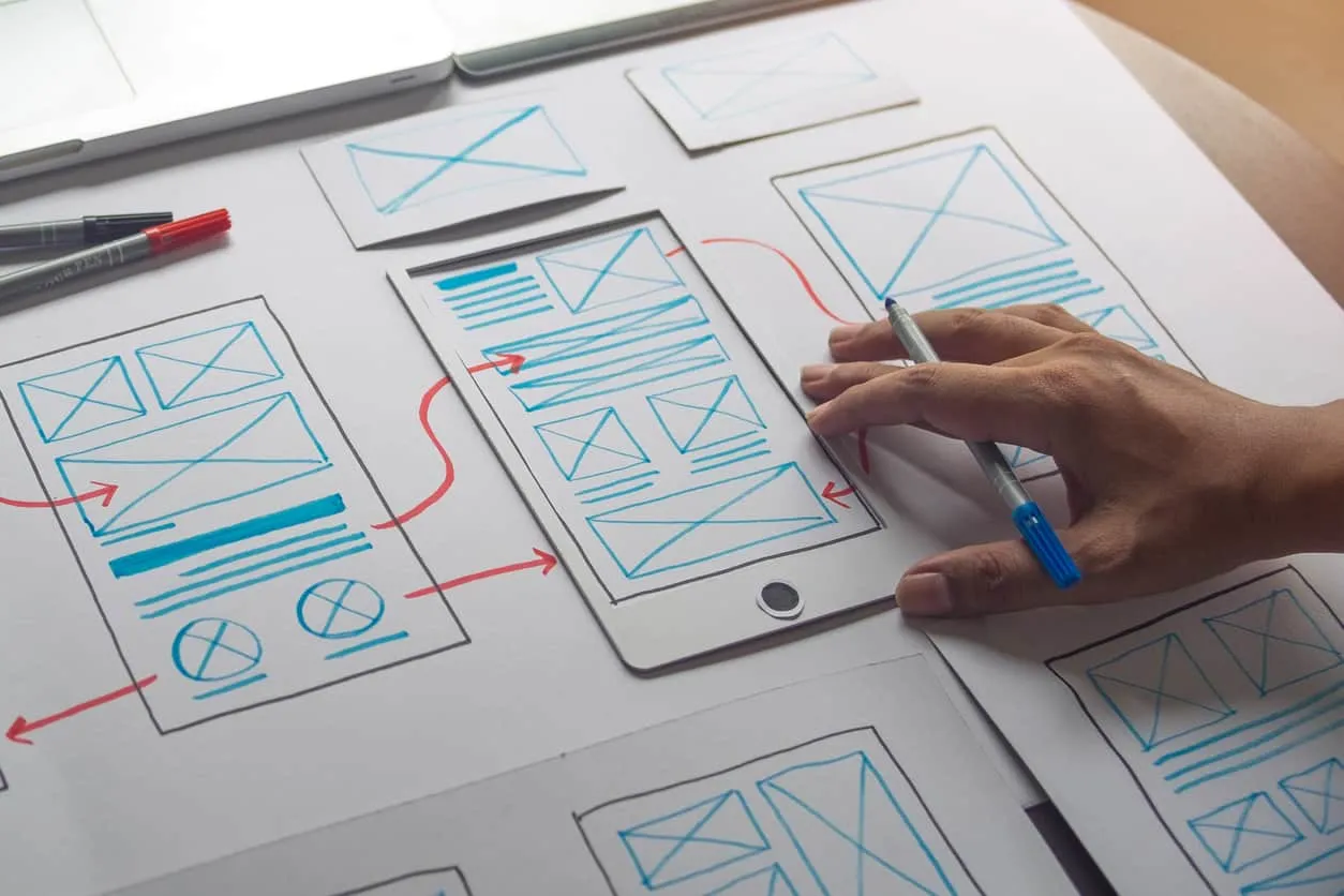A hand drawing page wireframes and flow arrows on printed sheets