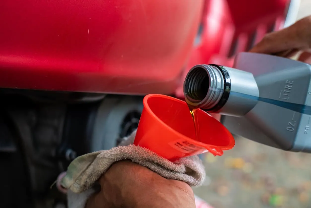 Oil being poured through a red funnel into an engine