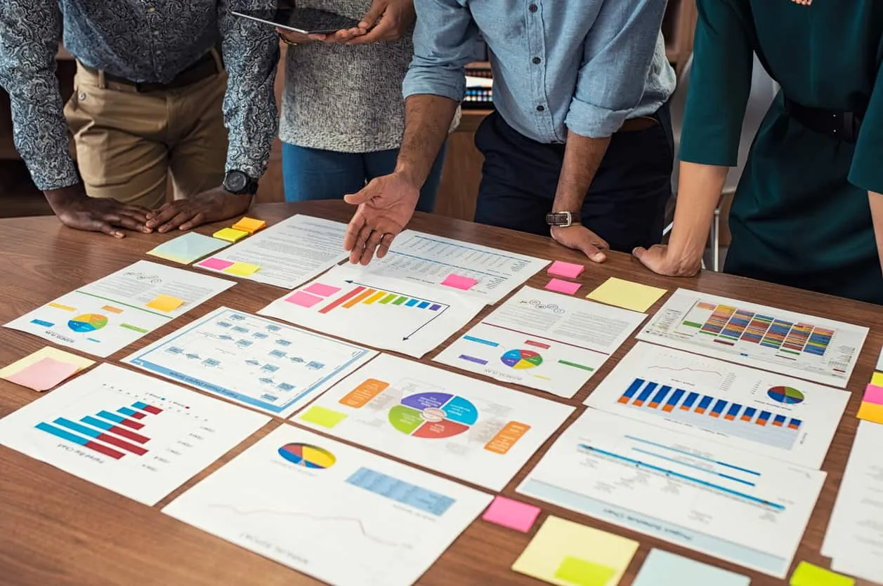 A team standing over a table spread with printed charts and sticky notes
