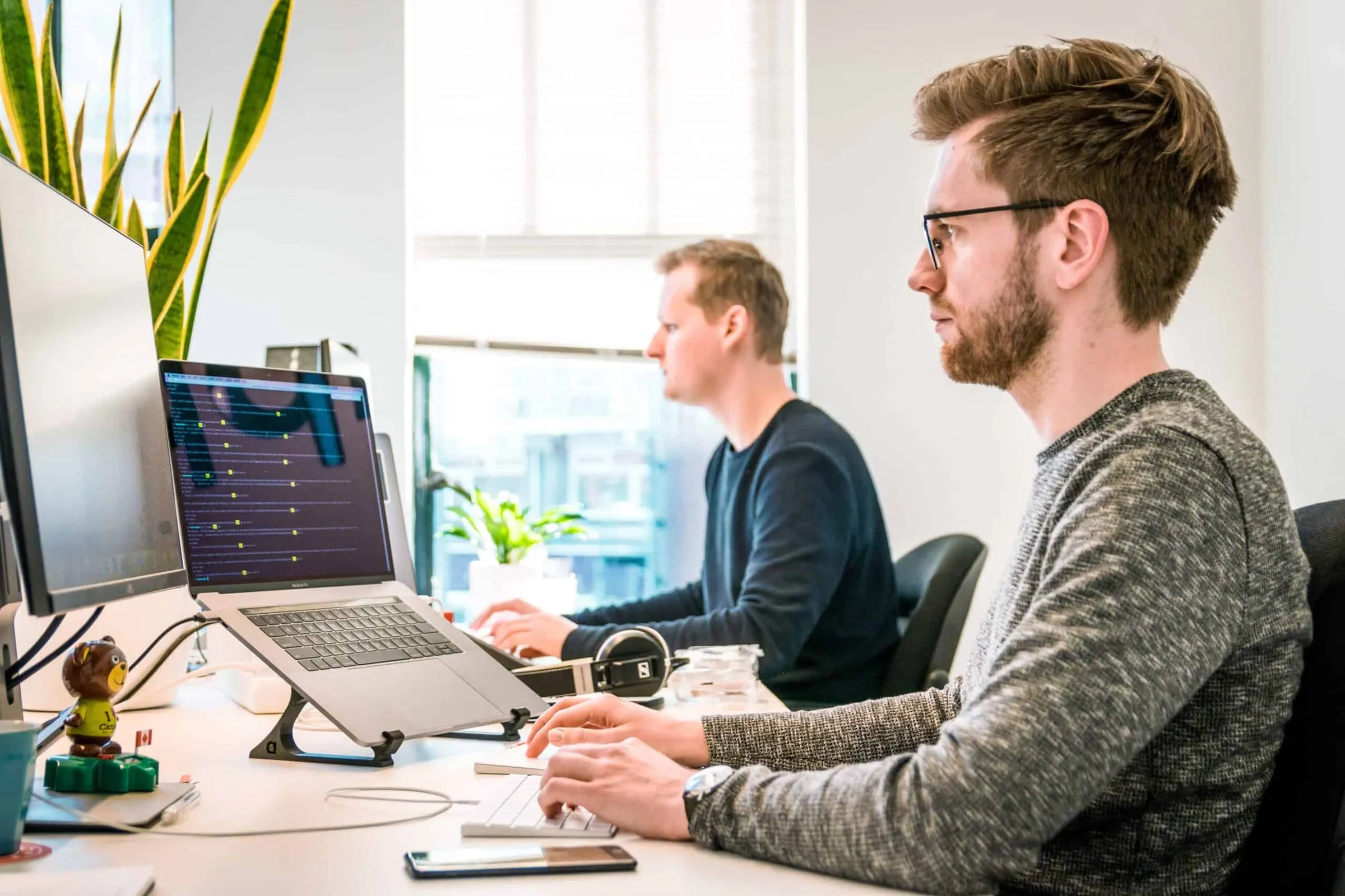 Two men working at desks with monitors in a bright office