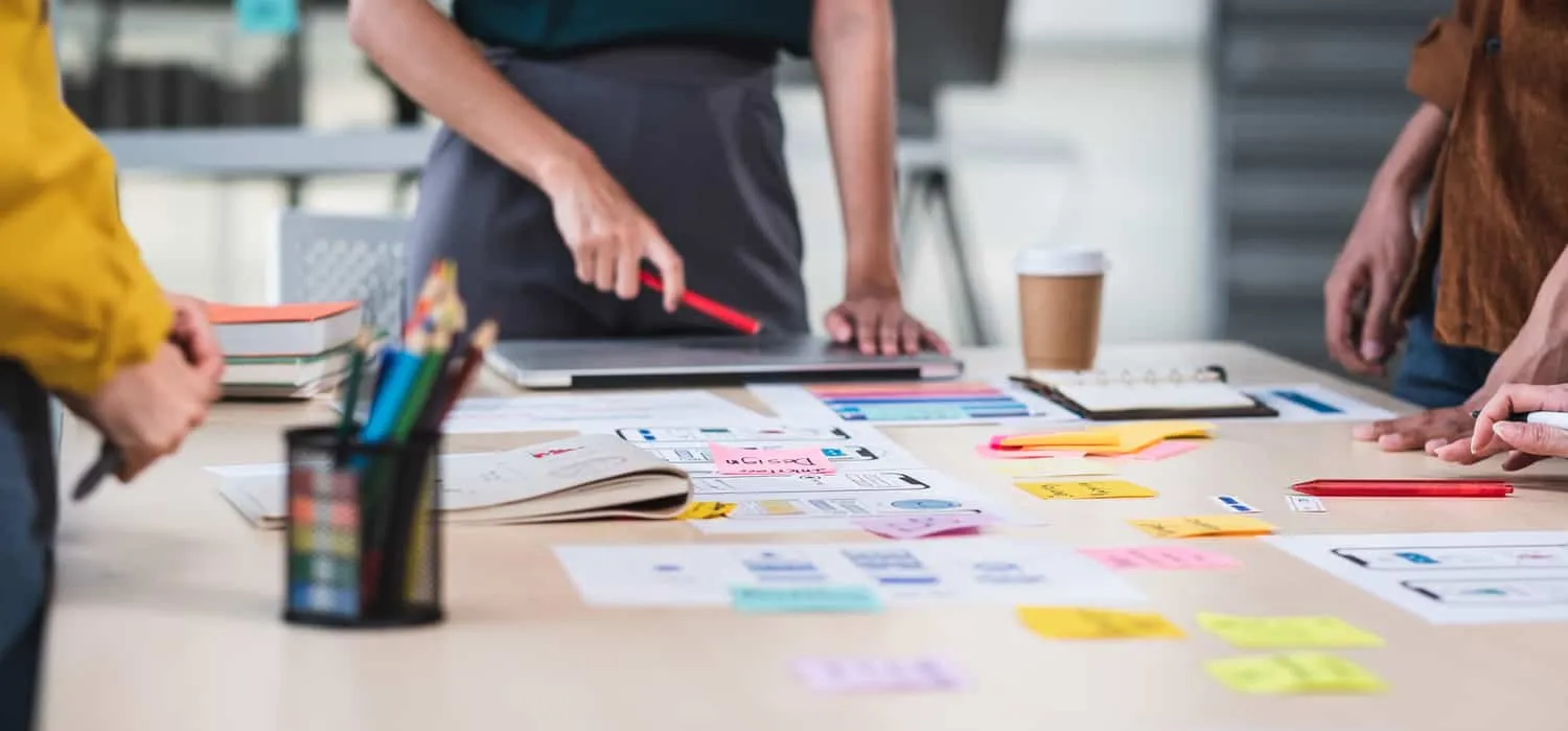 A team standing around a table covered in sticky notes, printouts and marker pens