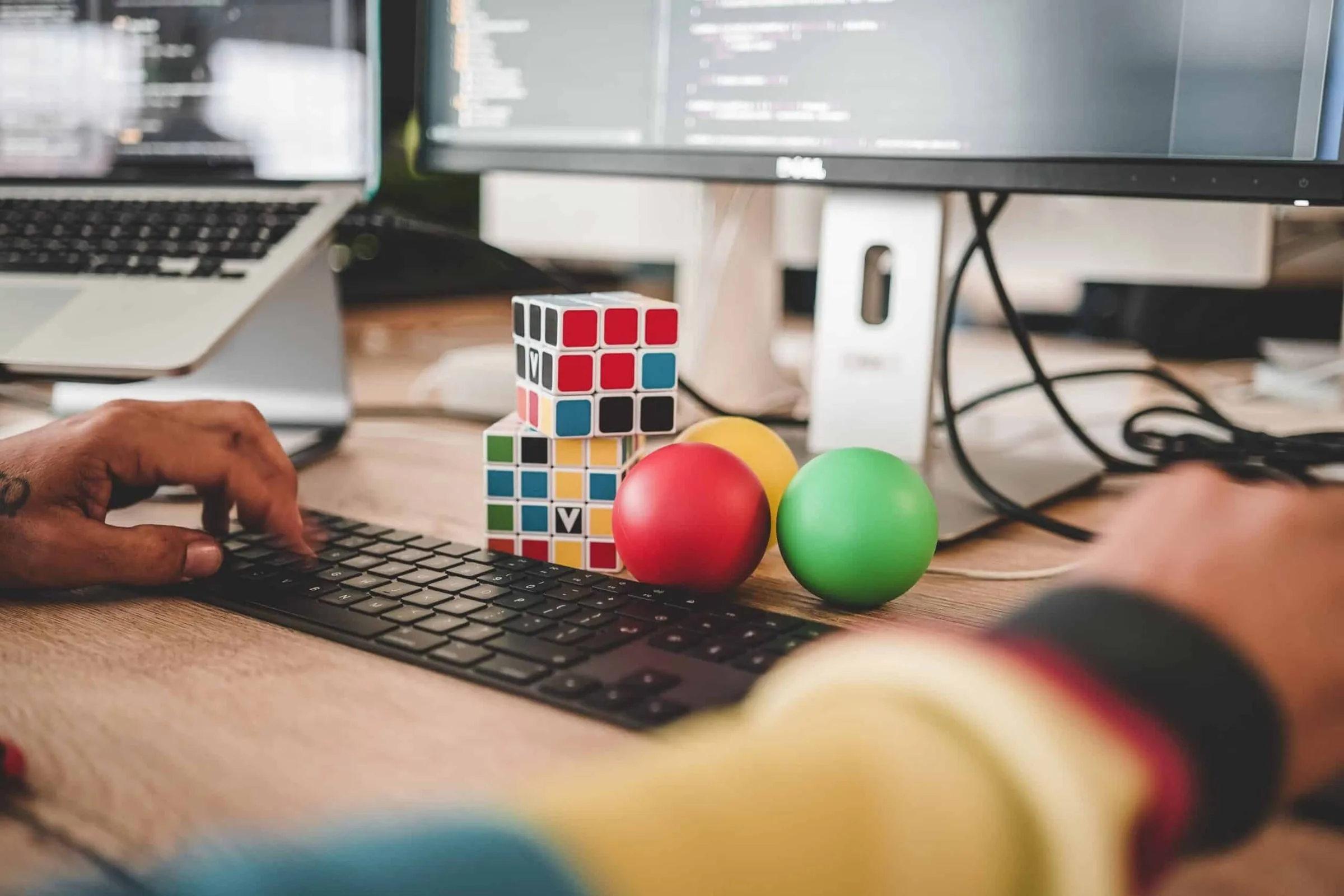 Hands typing at a keyboard beside a Rubik's cube and juggling balls