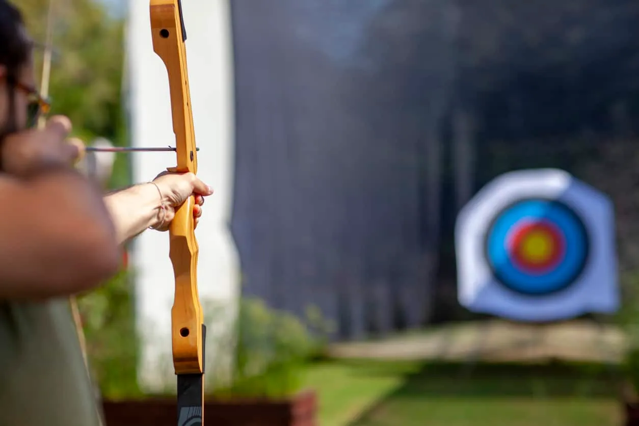 An archer drawing a bow with a target in the background