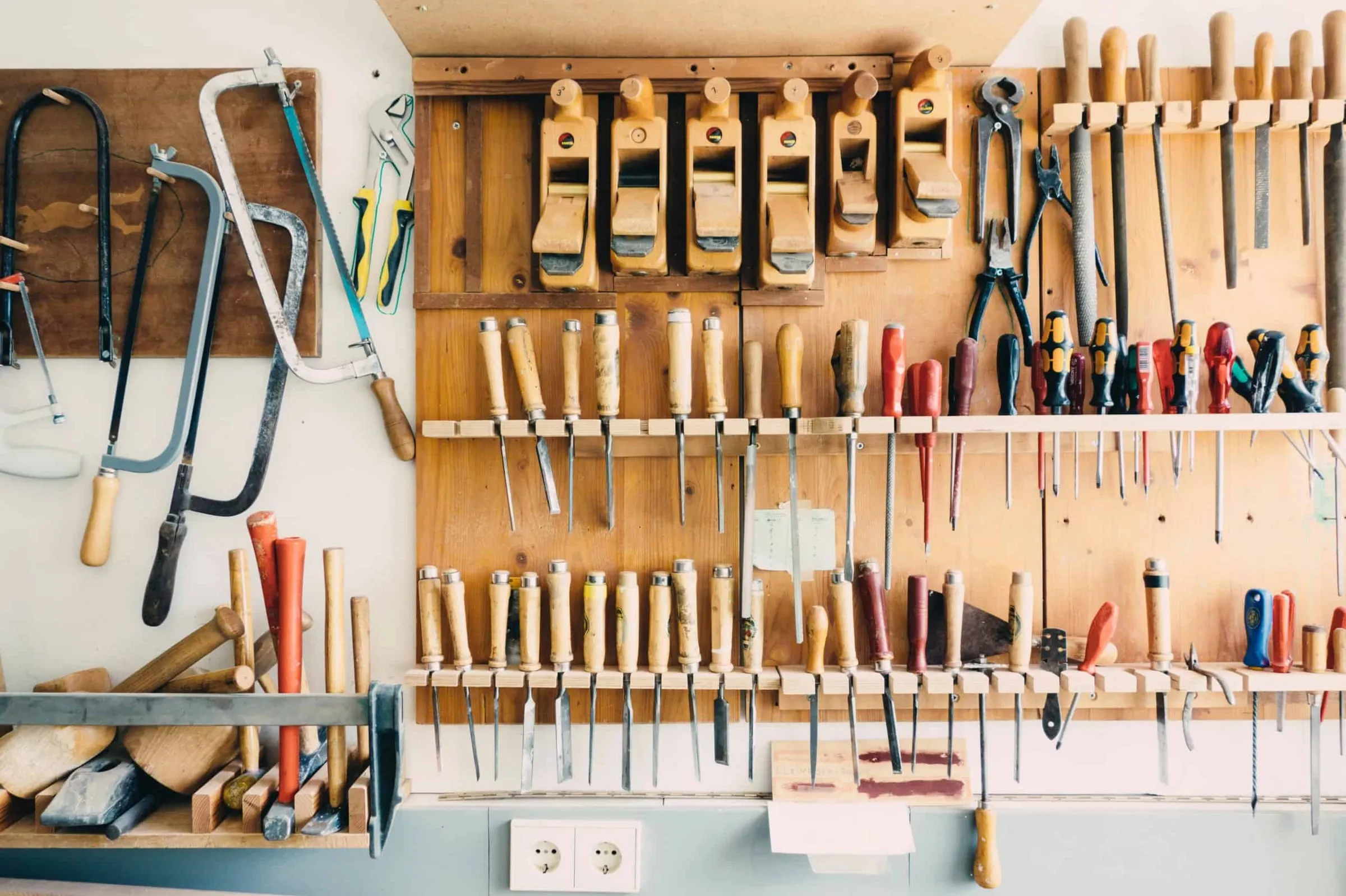 A workshop wall hung with woodworking tools above a bench