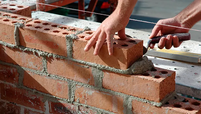 A bricklayer setting a brick into mortar along a guide line