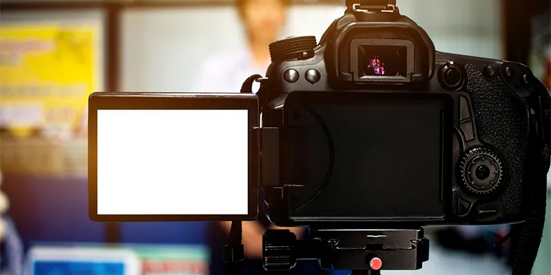 A DSLR camera on a tripod with its flip-out screen open, filming in a lit room