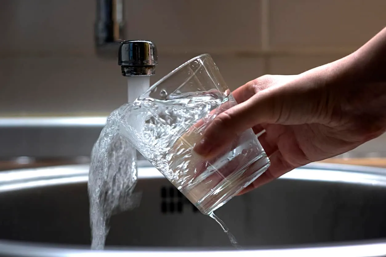A hand holding a glass overflowing under a running tap