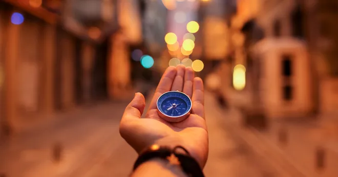 A hand holding a compass on a street lined with warm lights