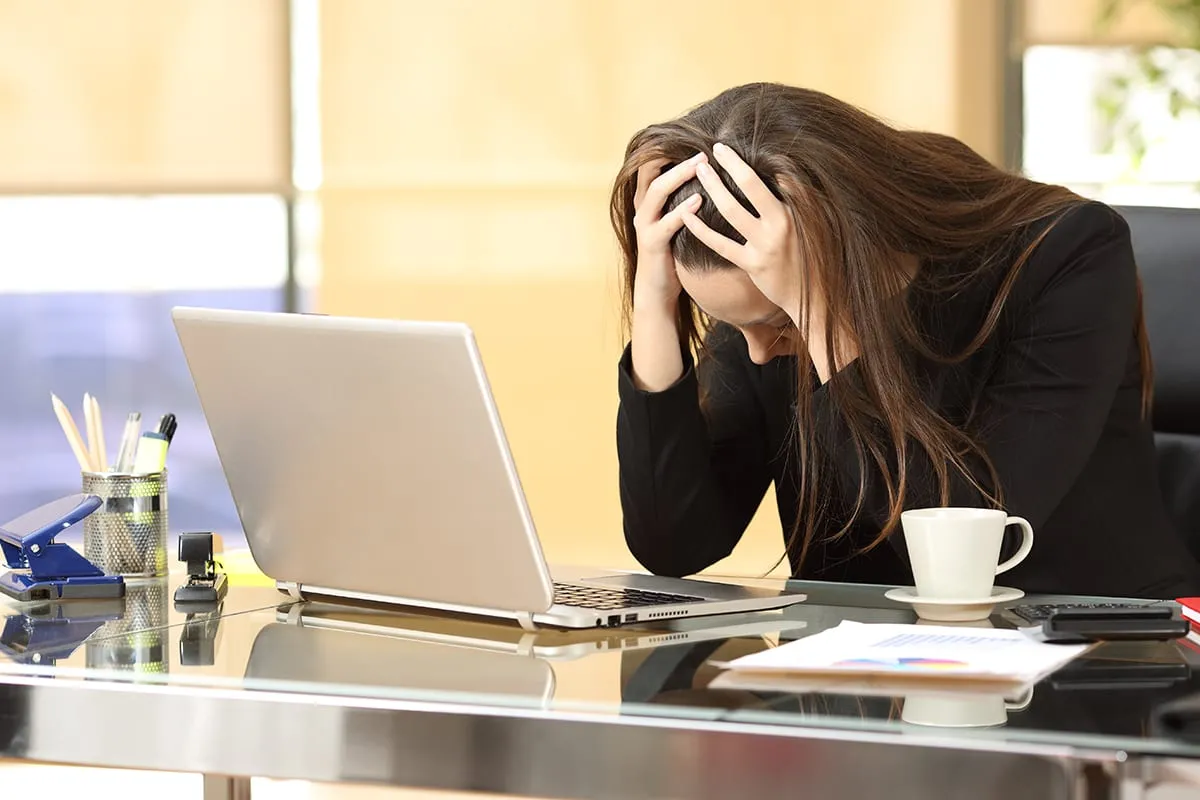 A woman holding her head in her hands in front of a laptop
