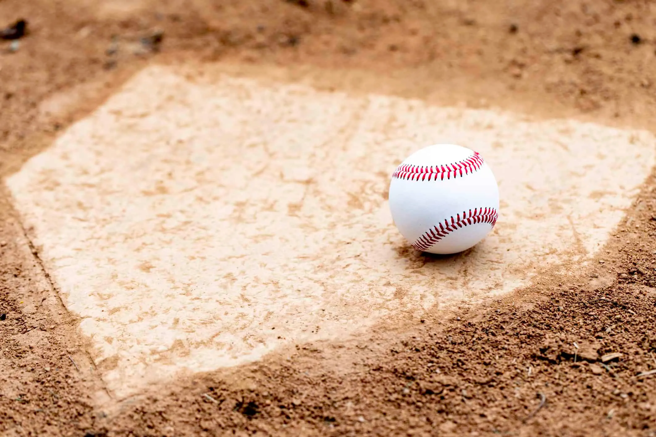 A baseball resting on home plate in the dirt