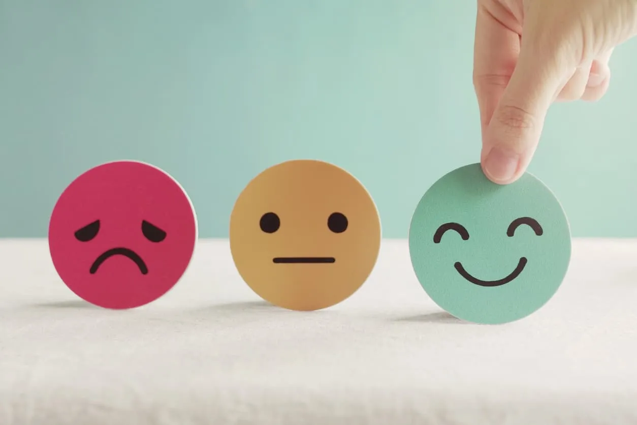 A hand choosing the smiling face from three cards showing sad, neutral and happy expressions