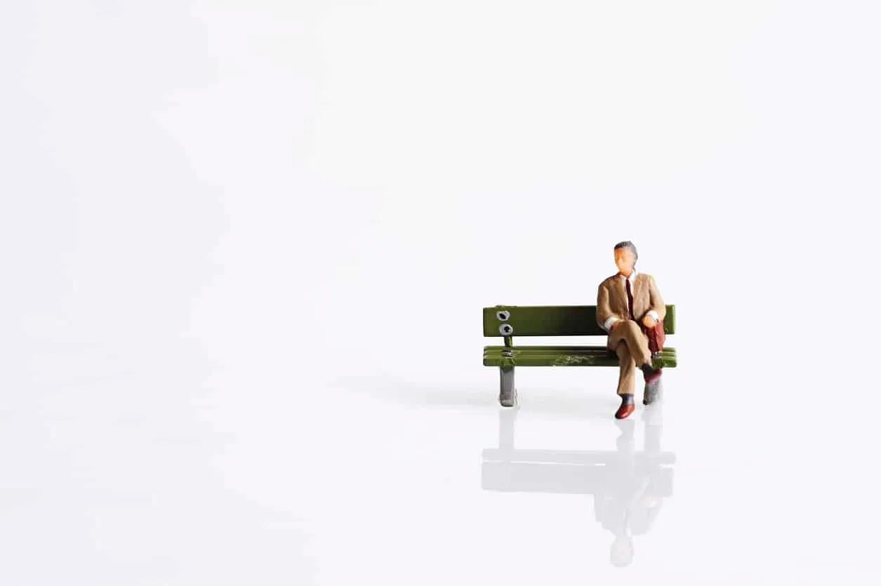 A tiny figure sitting alone on a bench in a vast white space