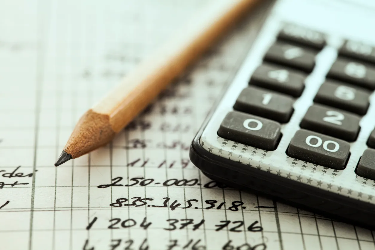 A pencil and calculator resting on a ledger of handwritten figures