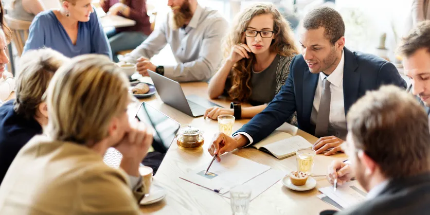 A group around a cafe table with laptops and coffee, mid discussion