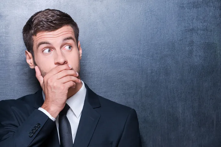 A man in a suit covering his mouth and looking sideways