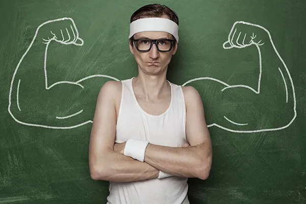 A thin man in a vest standing in front of a chalkboard drawing of muscular arms