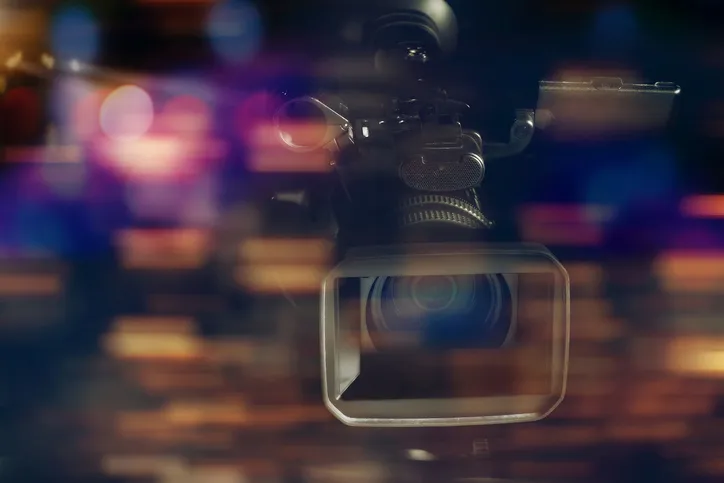 A television camera in a dark studio with blurred lights behind it
