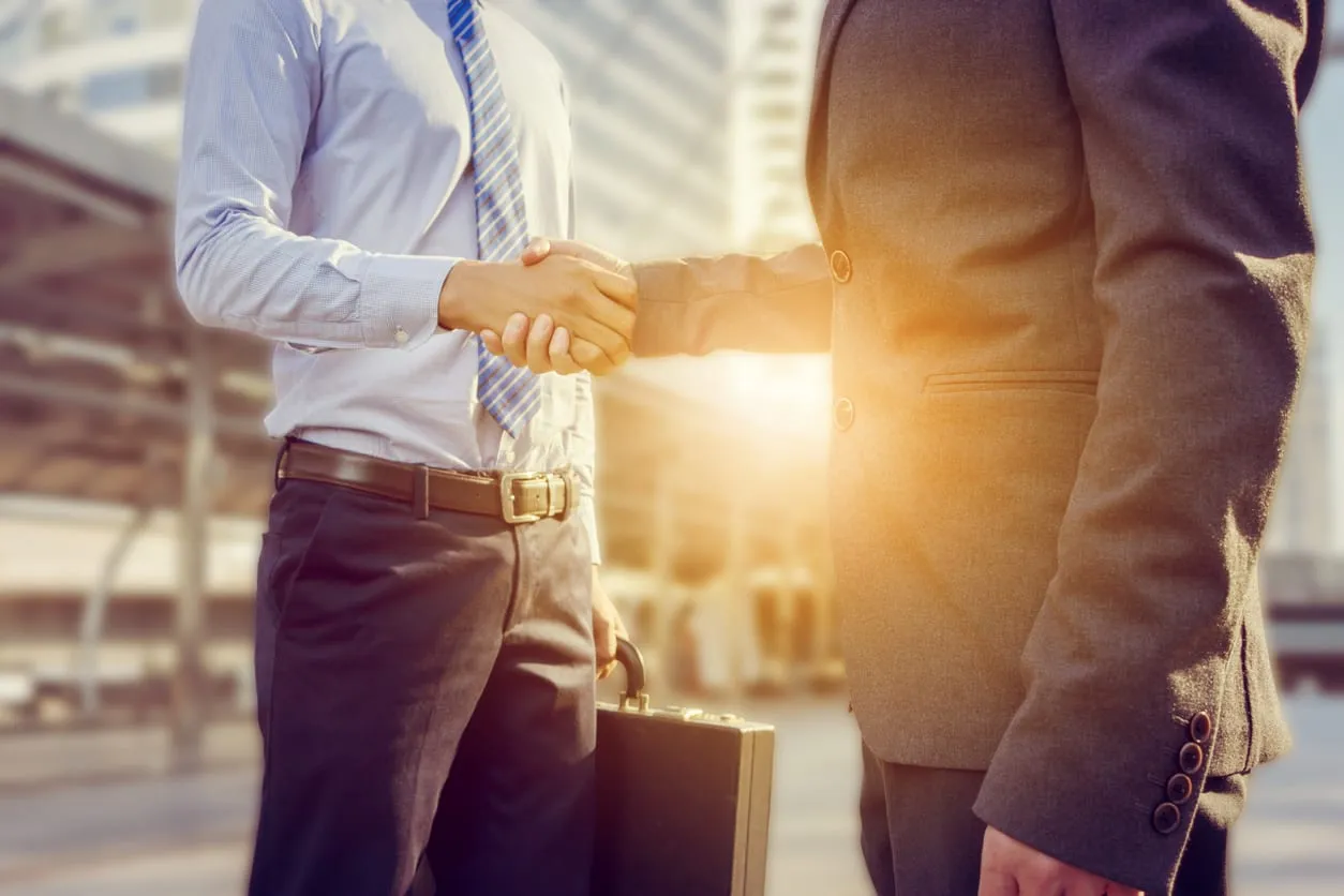 Two people in business dress shaking hands, one holding a briefcase