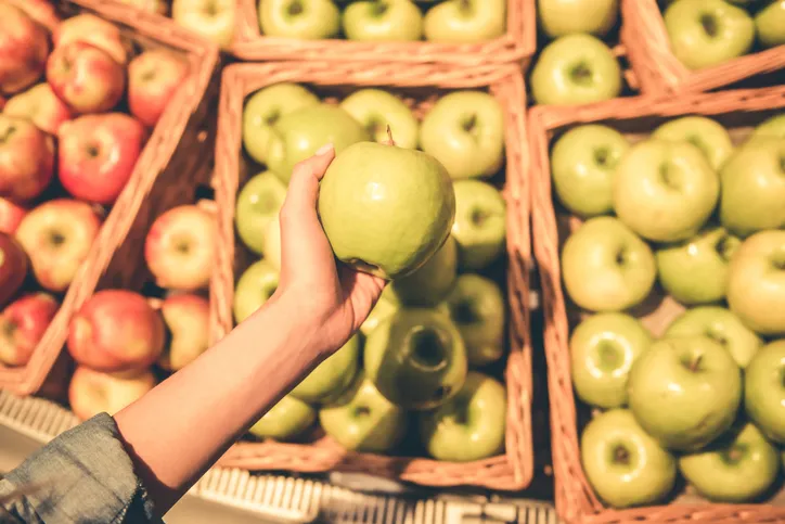 A hand picking a green apple from crates of apples at a market