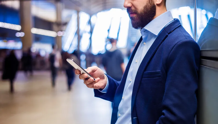 A man in a suit checking his phone in a busy transport hall