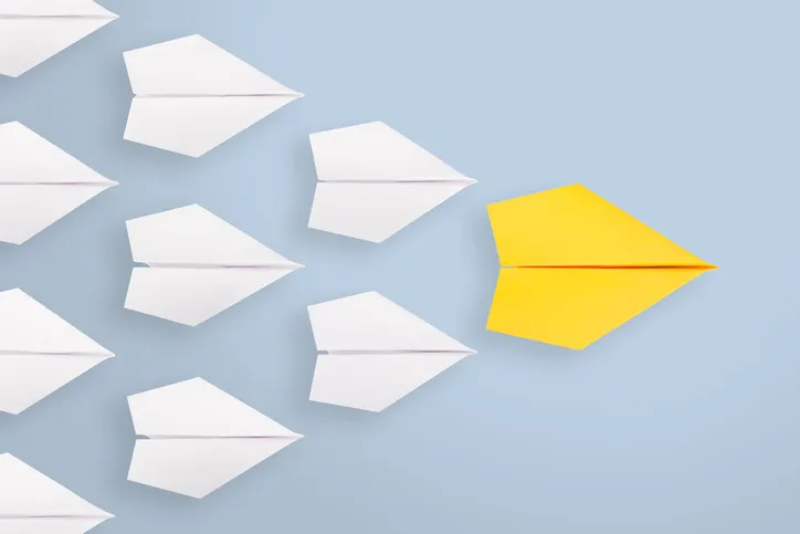 A yellow paper plane breaking away from a group of white ones