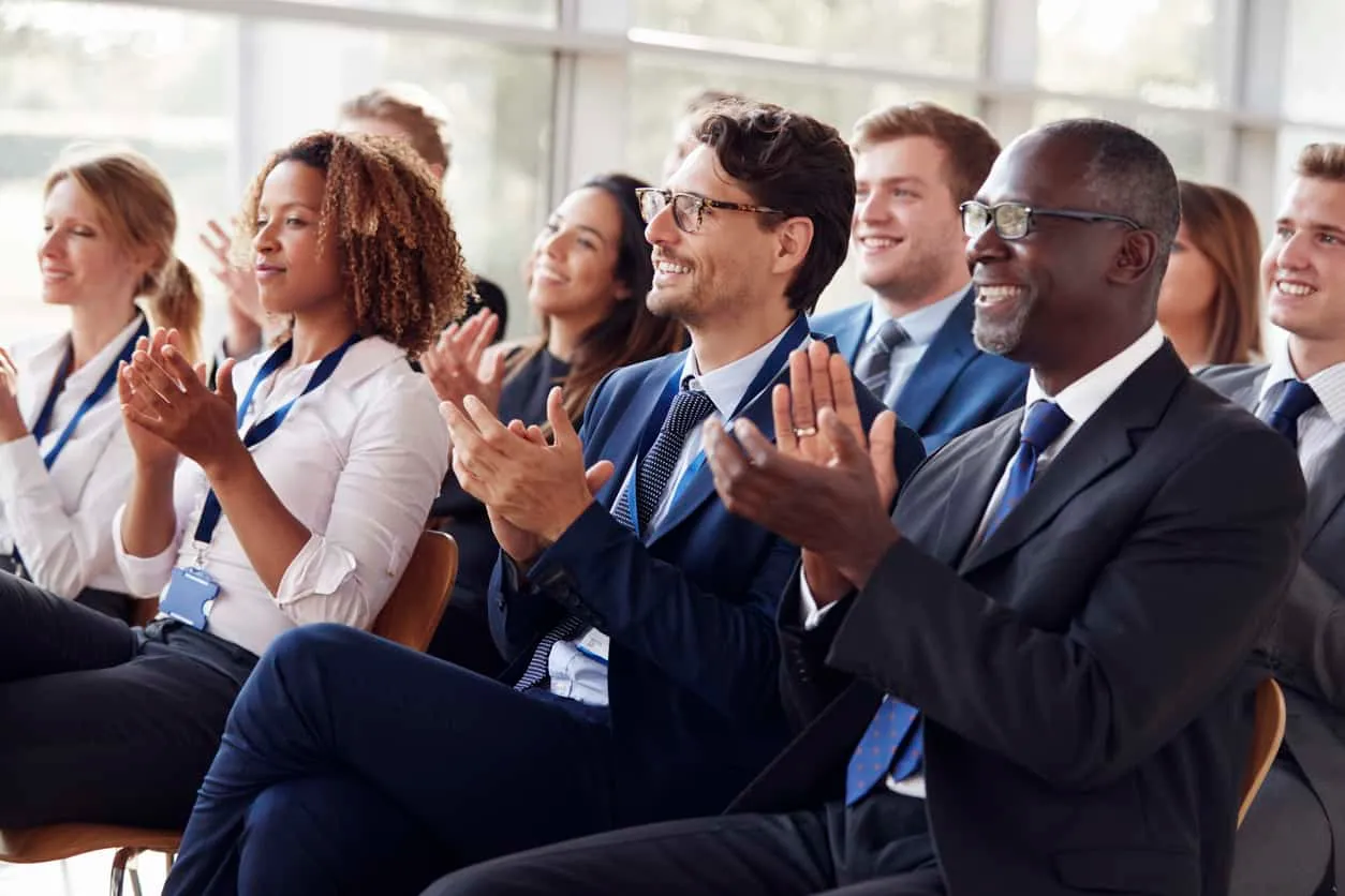 Rows of people in business dress applauding at a conference