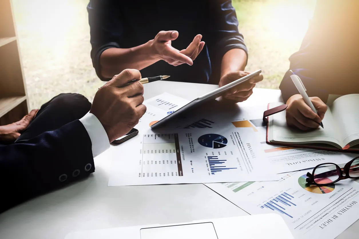 Two people reviewing printed charts across a desk, one gesturing as they talk