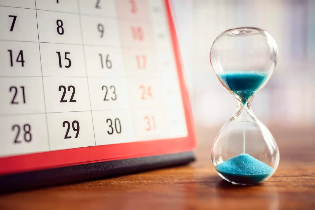 An hourglass with blue sand beside a wall calendar