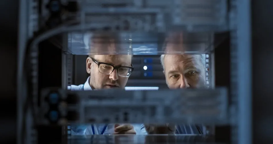 Two men studying equipment through the glass door of a server rack