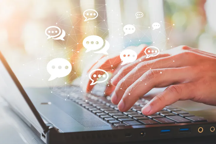 Hands typing on a laptop with speech bubble icons floating above the keyboard