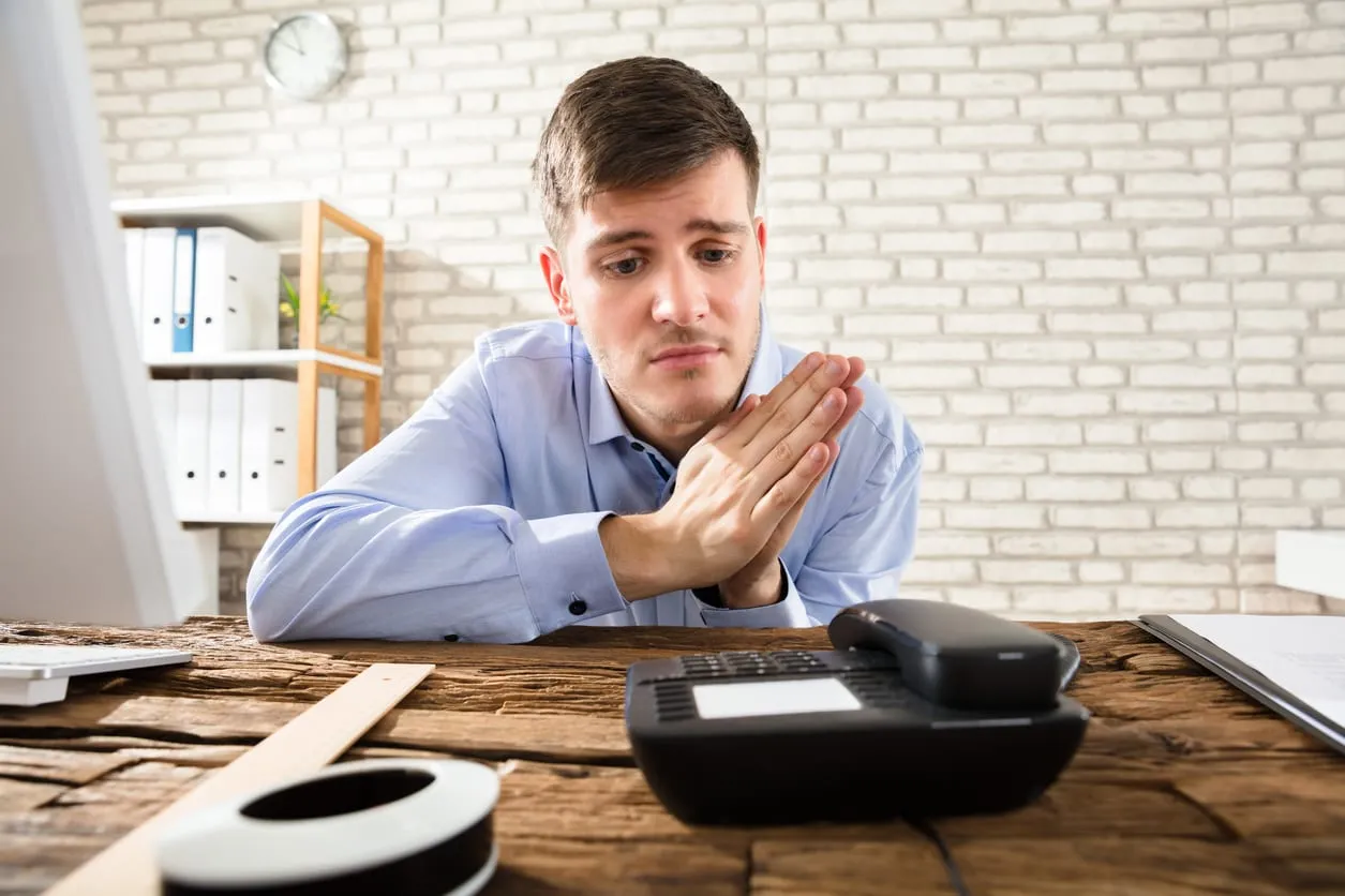 A man at a desk staring at a telephone, waiting for it to ring