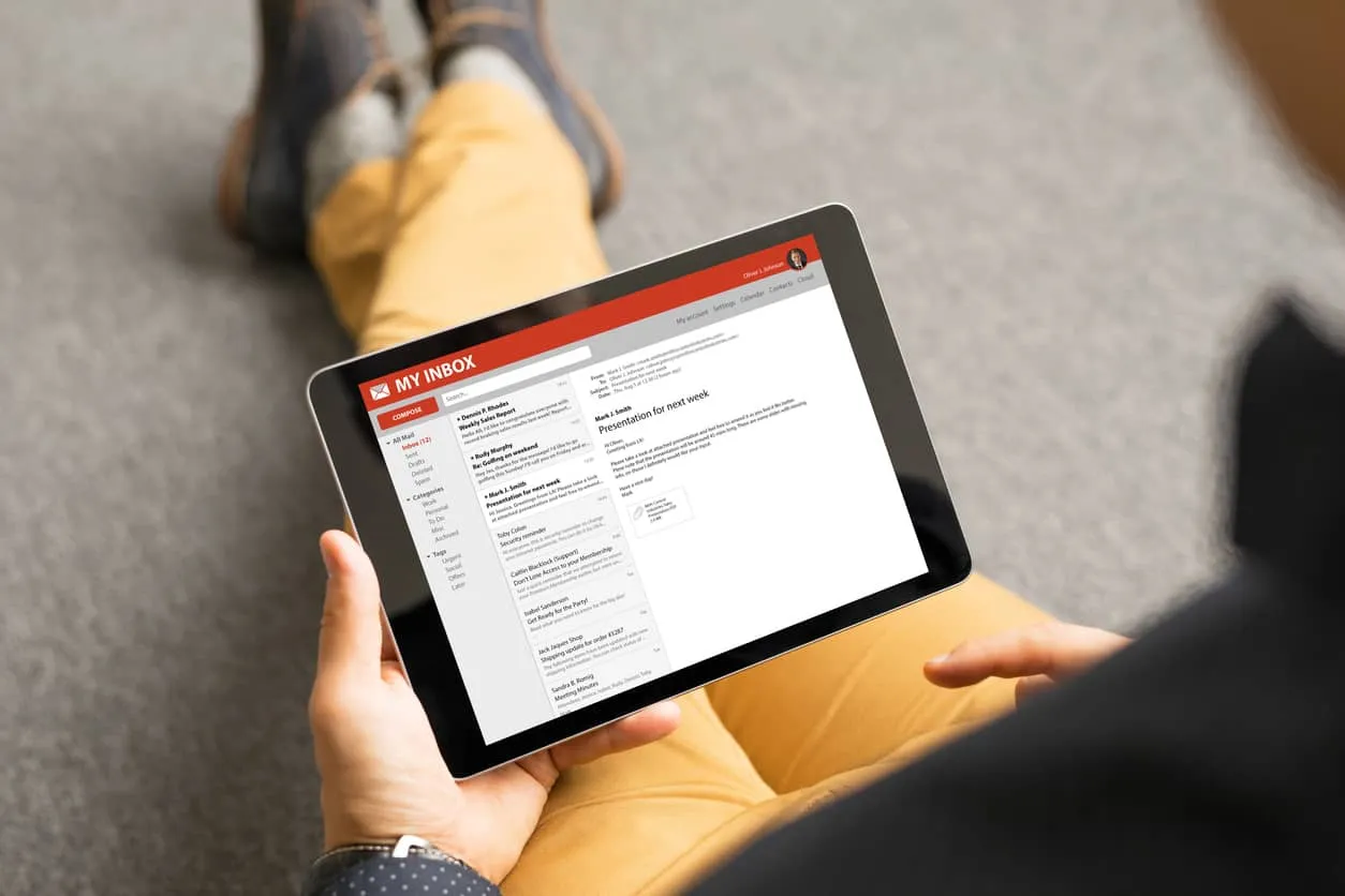 A person on a sofa reading an email inbox on a tablet