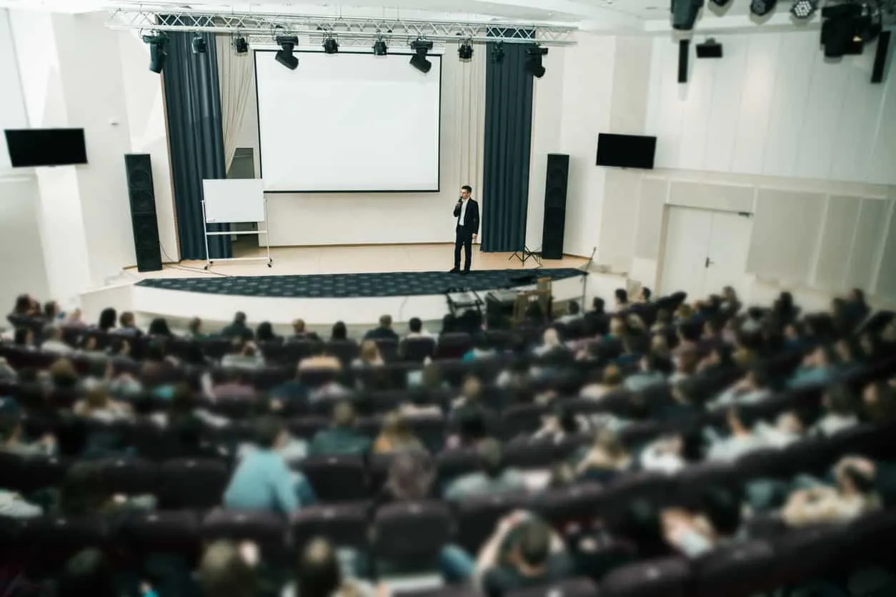 A single speaker on stage in front of a full auditorium