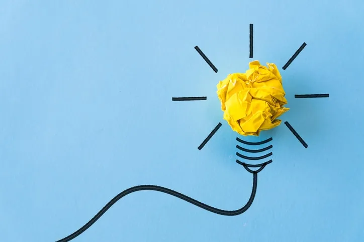 A crumpled yellow paper ball drawn as the bulb of a light bulb on blue paper