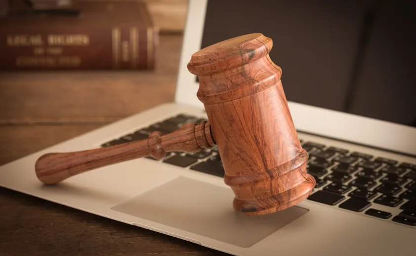 A wooden gavel resting on an open laptop beside a law book