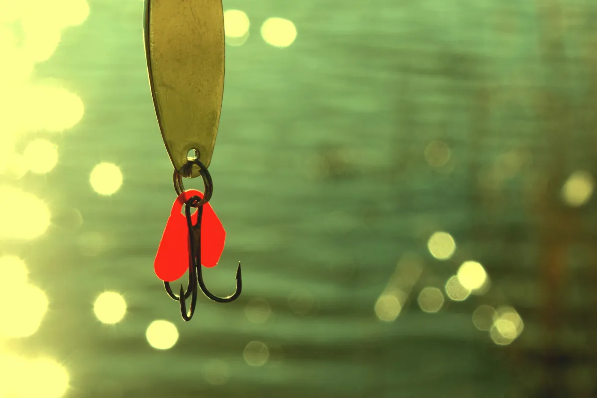 A fishing lure with a red tail and treble hook against a green background