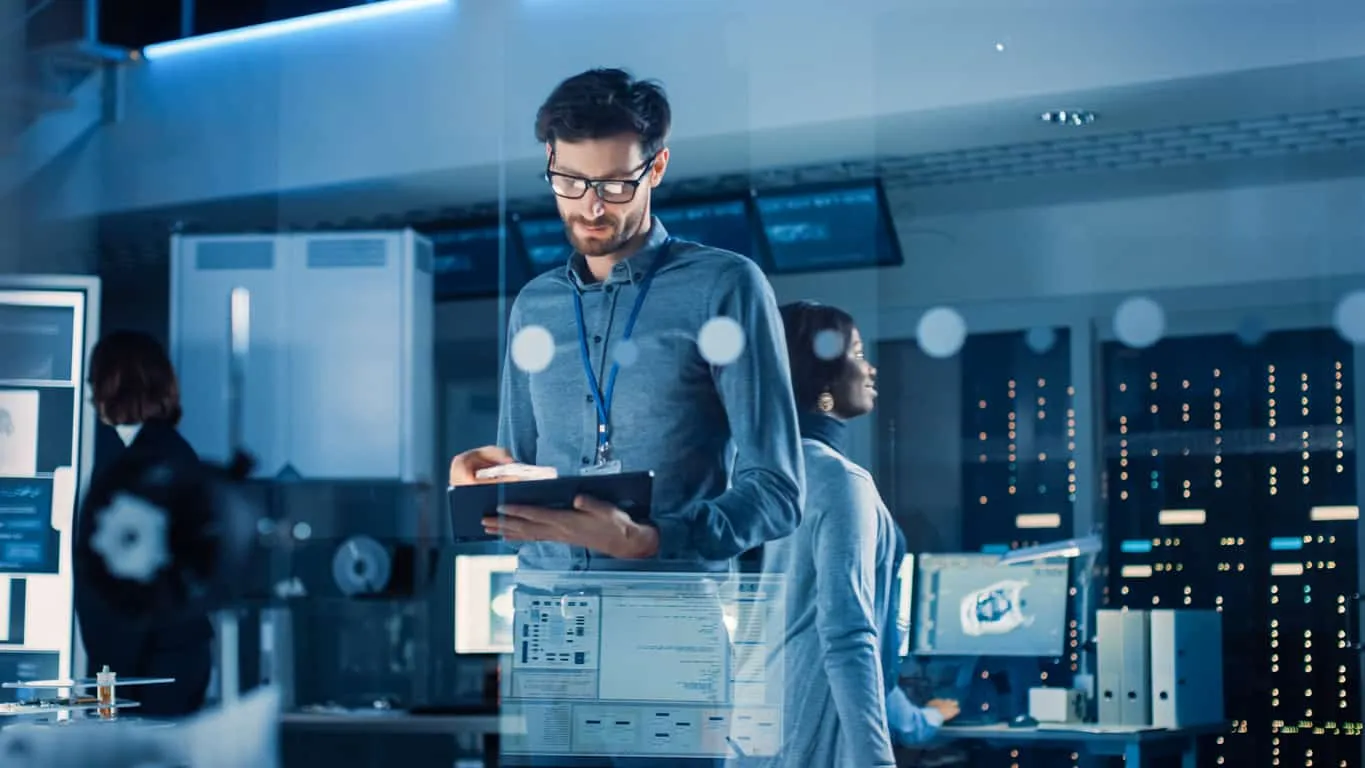 A man in glasses holding a tablet in a server room, with data overlaid