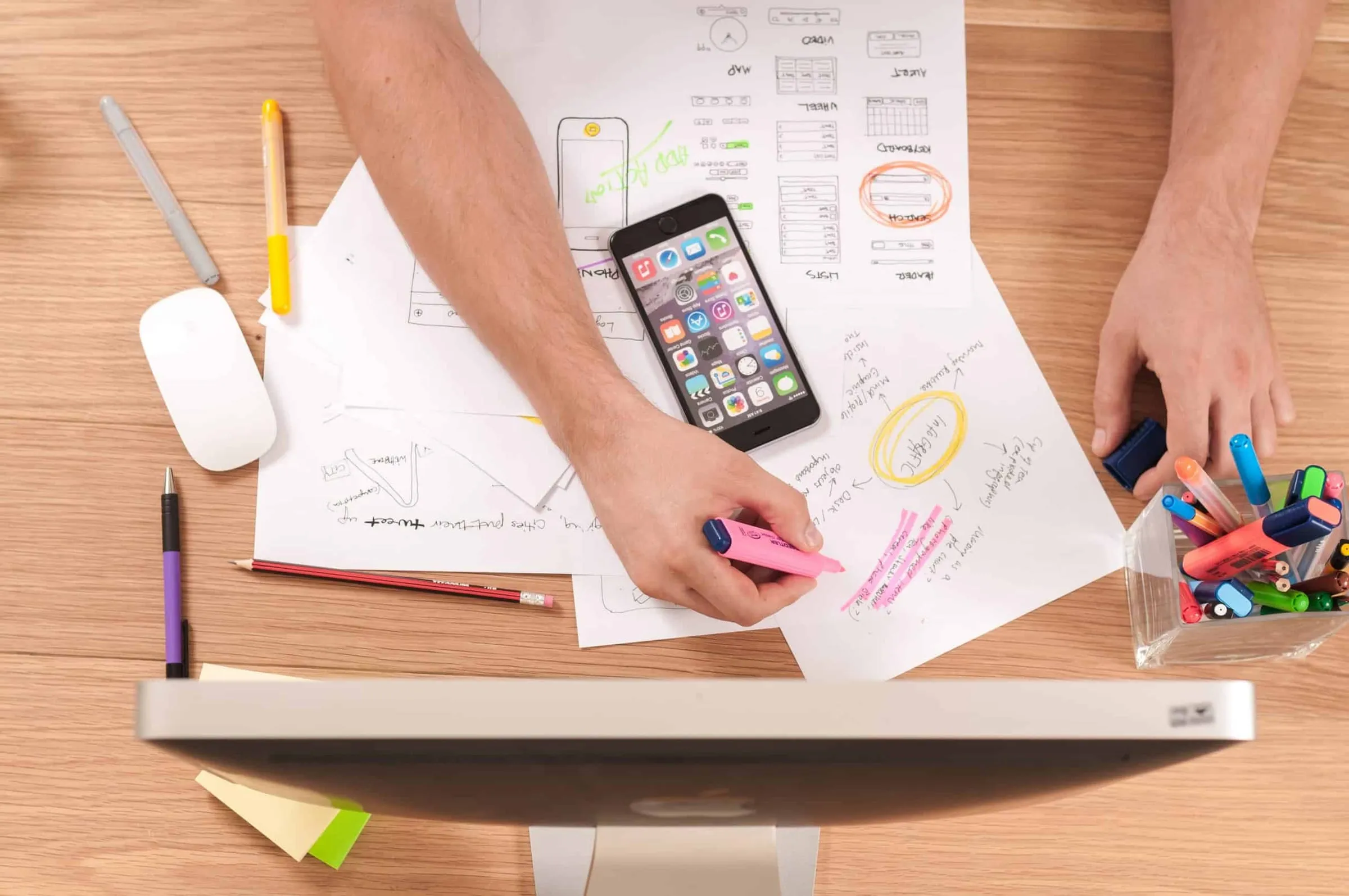 Overhead view of hands annotating printed pages beside a phone, pens and highlighters