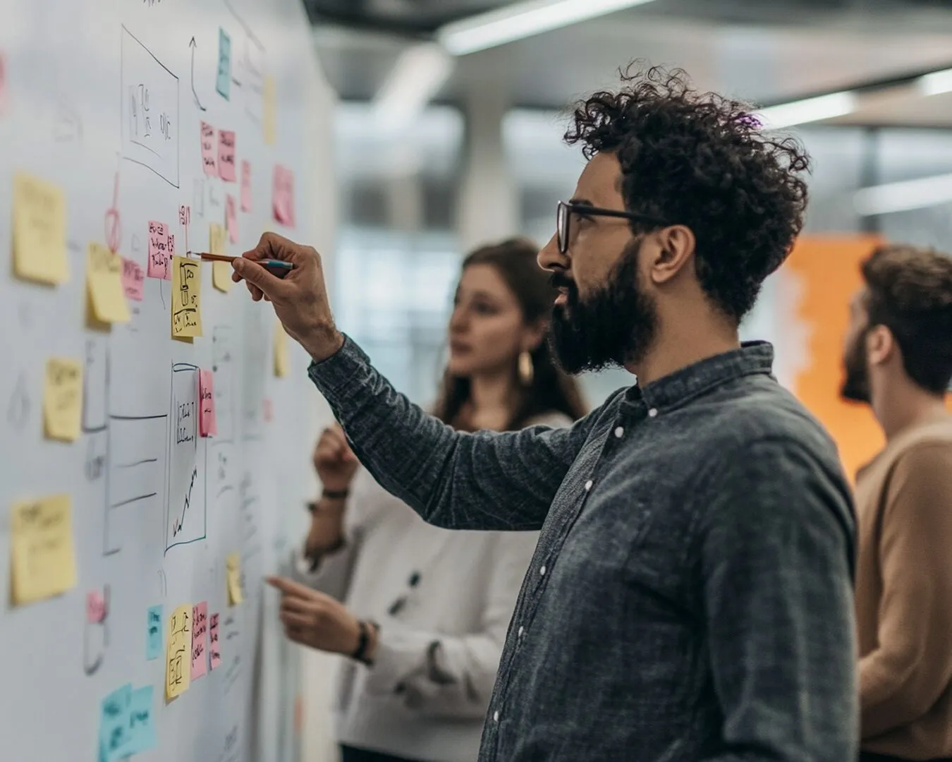 A man writing on a wall covered in sticky notes while colleagues watch