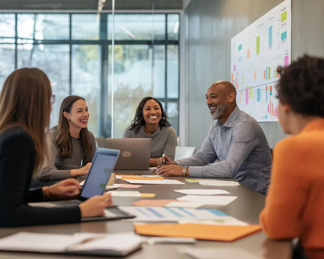 Five colleagues talking around a meeting table with a planning board on the wall behind them