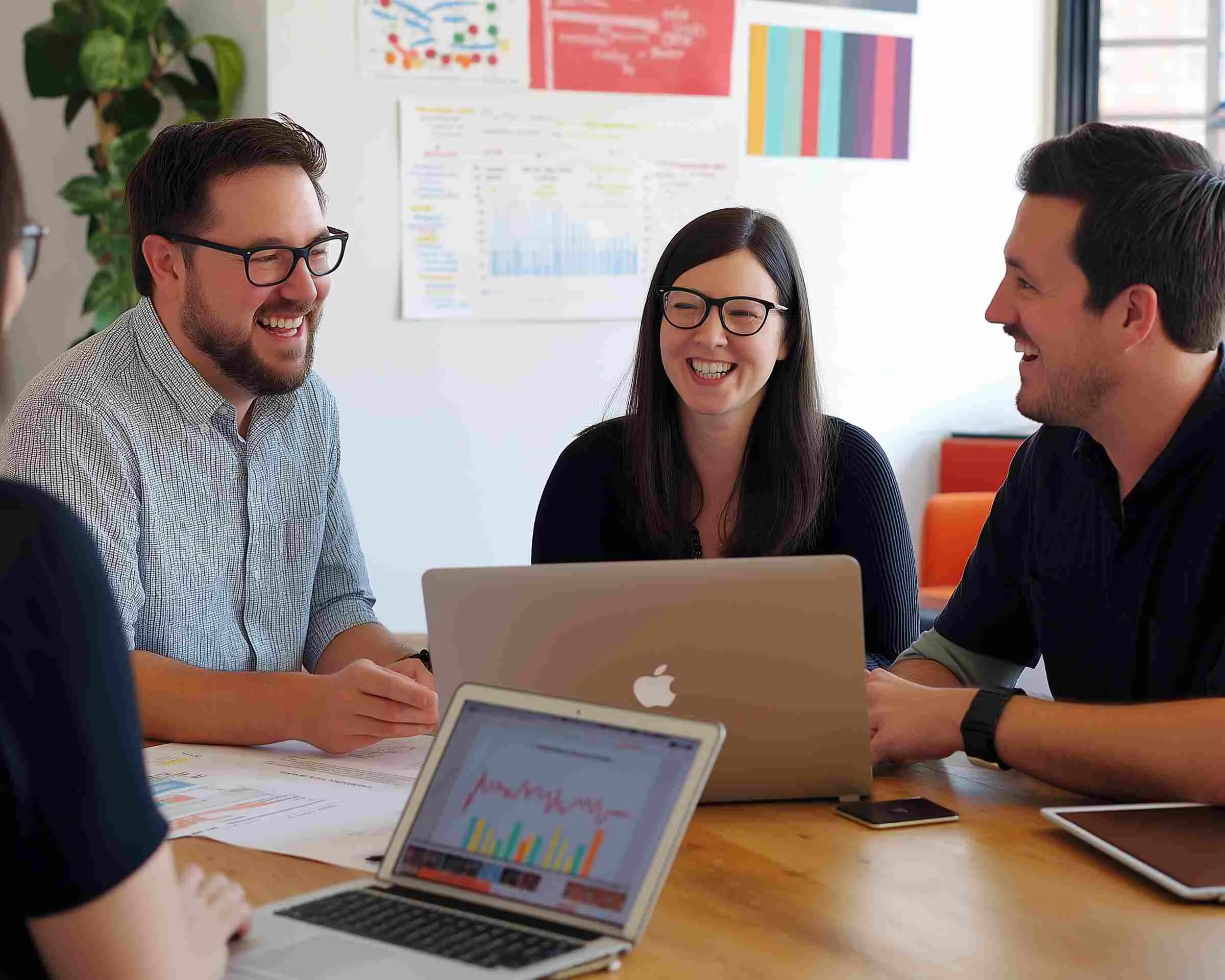 Three colleagues laughing around a laptop at a meeting table