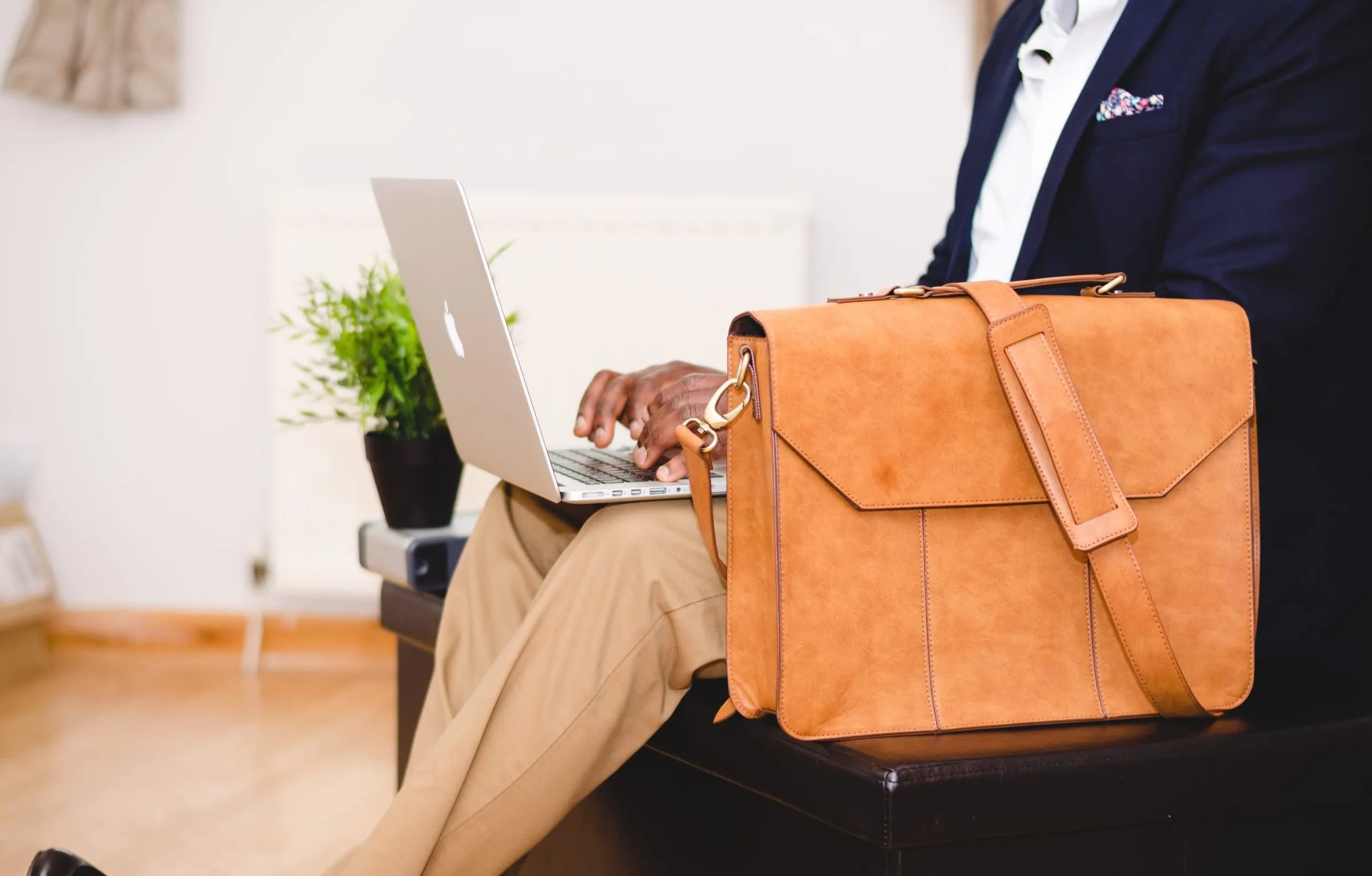 A person working at a laptop beside a tan leather briefcase