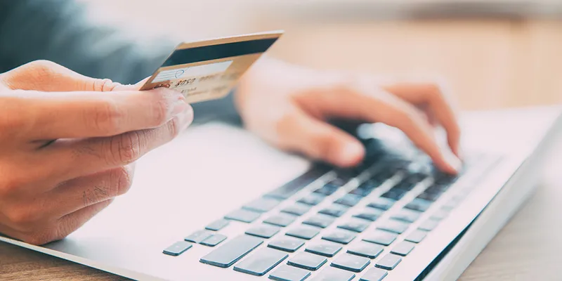 A hand holding a credit card while typing on a laptop