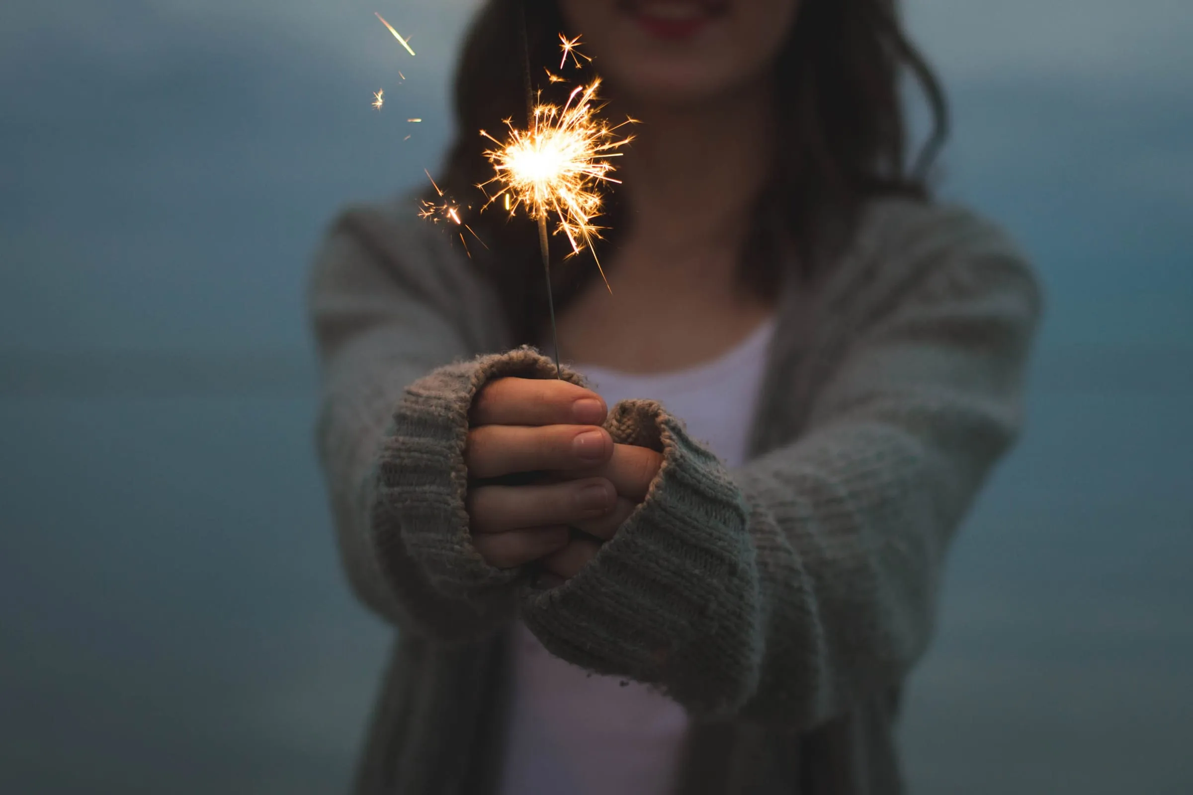 A person holding a lit sparkler out towards the camera