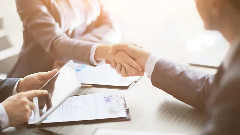 Two people shaking hands over a desk of printed charts
