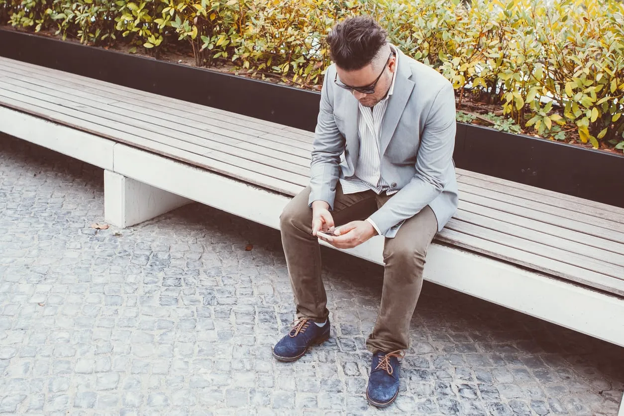 A man in a jacket sitting on a bench looking at his phone