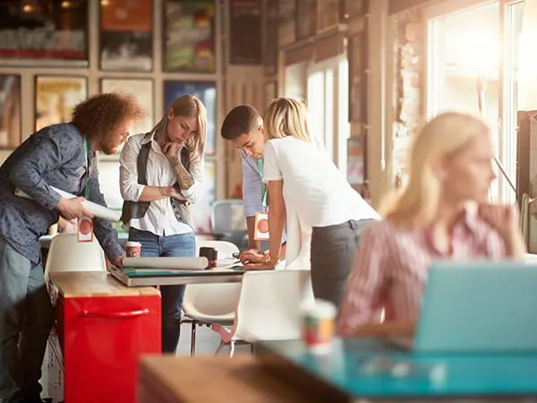 A team gathered around a table in a cafe, talking over printouts and laptops