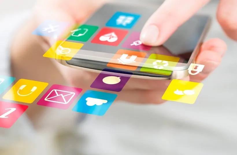 A hand holding a phone with colourful social media app icons floating above the screen