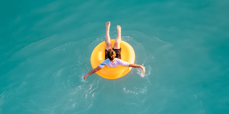 Overhead view of a person floating on a yellow ring in turquoise water